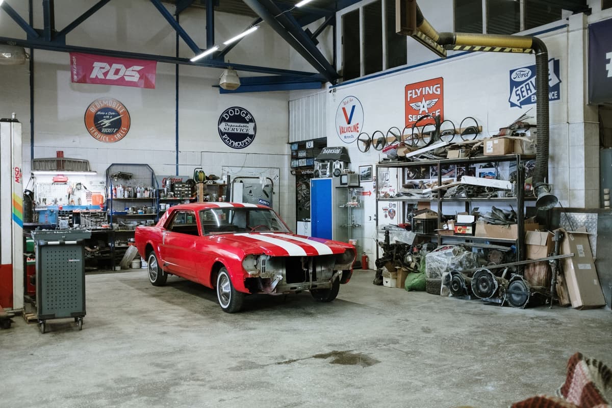 A vintage car being worked on in a workshop stocked with tools and parts